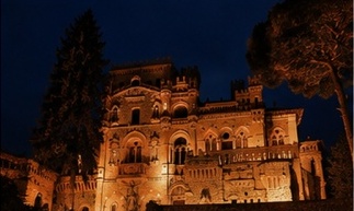 Le Castello della Monica illuminé de nuit, sa silhouette néo-médiévale se détachant sur le ciel sombre.