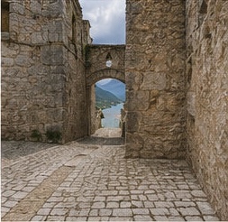 Une ruelle pavée voûtée du bourg médiéval de Barrea, avec vue sur le lac au loin.