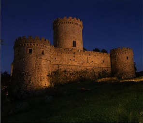Le Castello Piccolomini di Ortucchio éclairé de nuit, ses tours se détachant sur le ciel sombre.