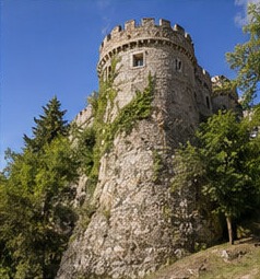 Une tour ronde crénelée du Castello Piccolomini di Ortucchio, entourée d'arbres.