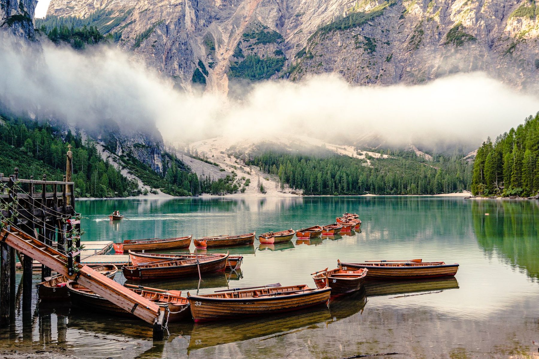Les barques en bois du Lago di Braies, dans les Dolomites, entourées de montagnes et de brume.