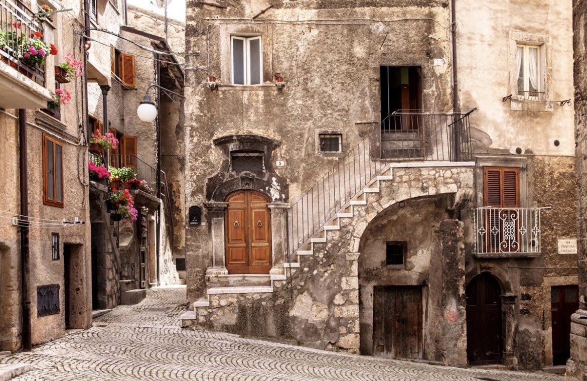 Ruelle pavée de Pacentro avec un escalier de pierre et des géraniums aux fenêtres.
