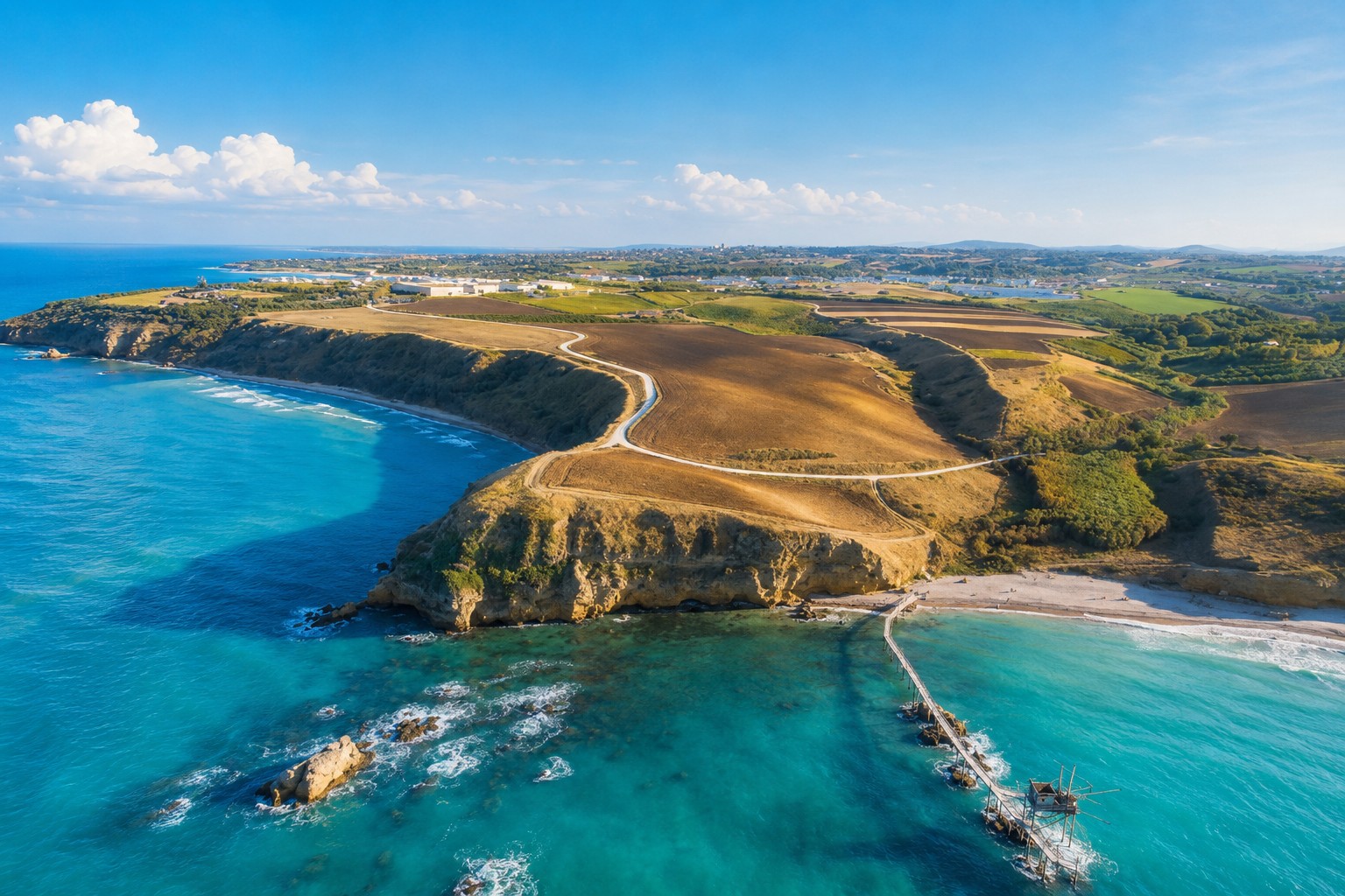 Vue aérienne de la Riserva di Punta Aderci : promontoire sauvage, plage en corniche et trabocco sur pilotis dans une mer turquoise.