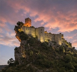 Le Castello di Roccascalegna illuminé au crépuscule, silhouette se détachant sur un ciel orangé.