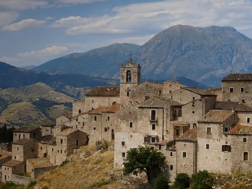 Illustration du village de Santo Stefano di Sessanio, ses toits de pierre et sa tour médicéenne, face aux montagnes du Gran Sasso.