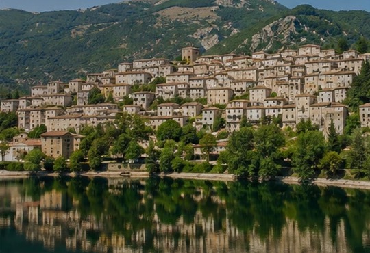 Illustration du village de Scanno accroché à la colline, ses maisons serrées et sa montagne en toile de fond, reflétés dans le lac de Scanno.