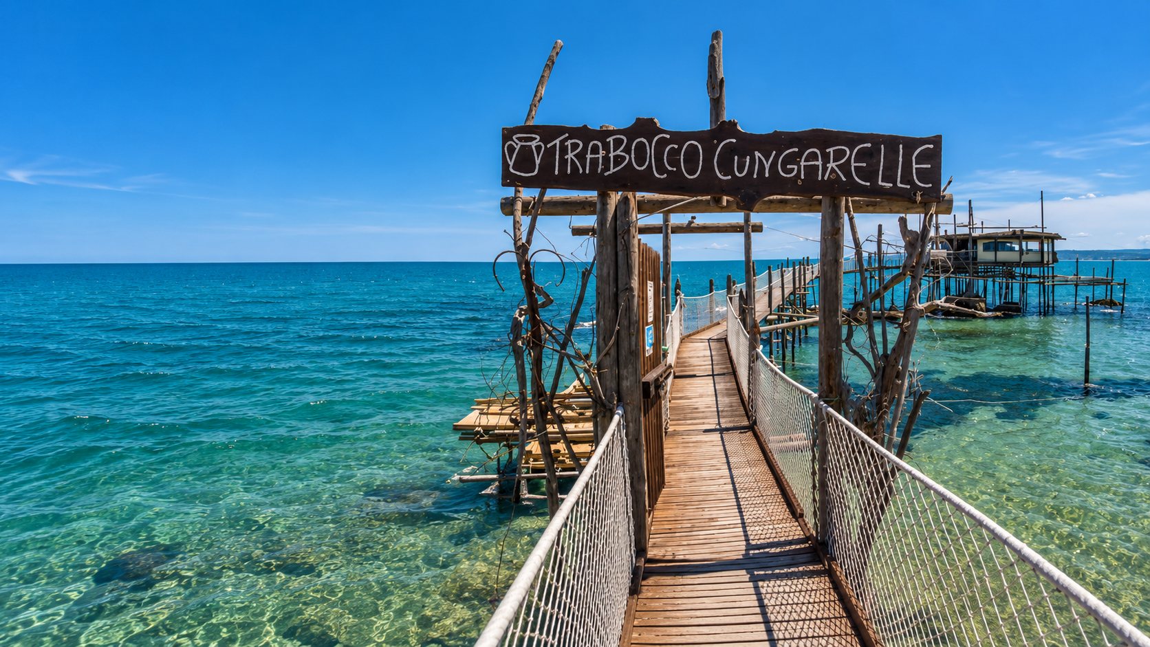 L'entrée du Trabocco Cungarelle à Vasto : une passerelle en bois sous une enseigne à son nom, au-dessus d'une eau turquoise, avec la cabane du trabocco au fond.
