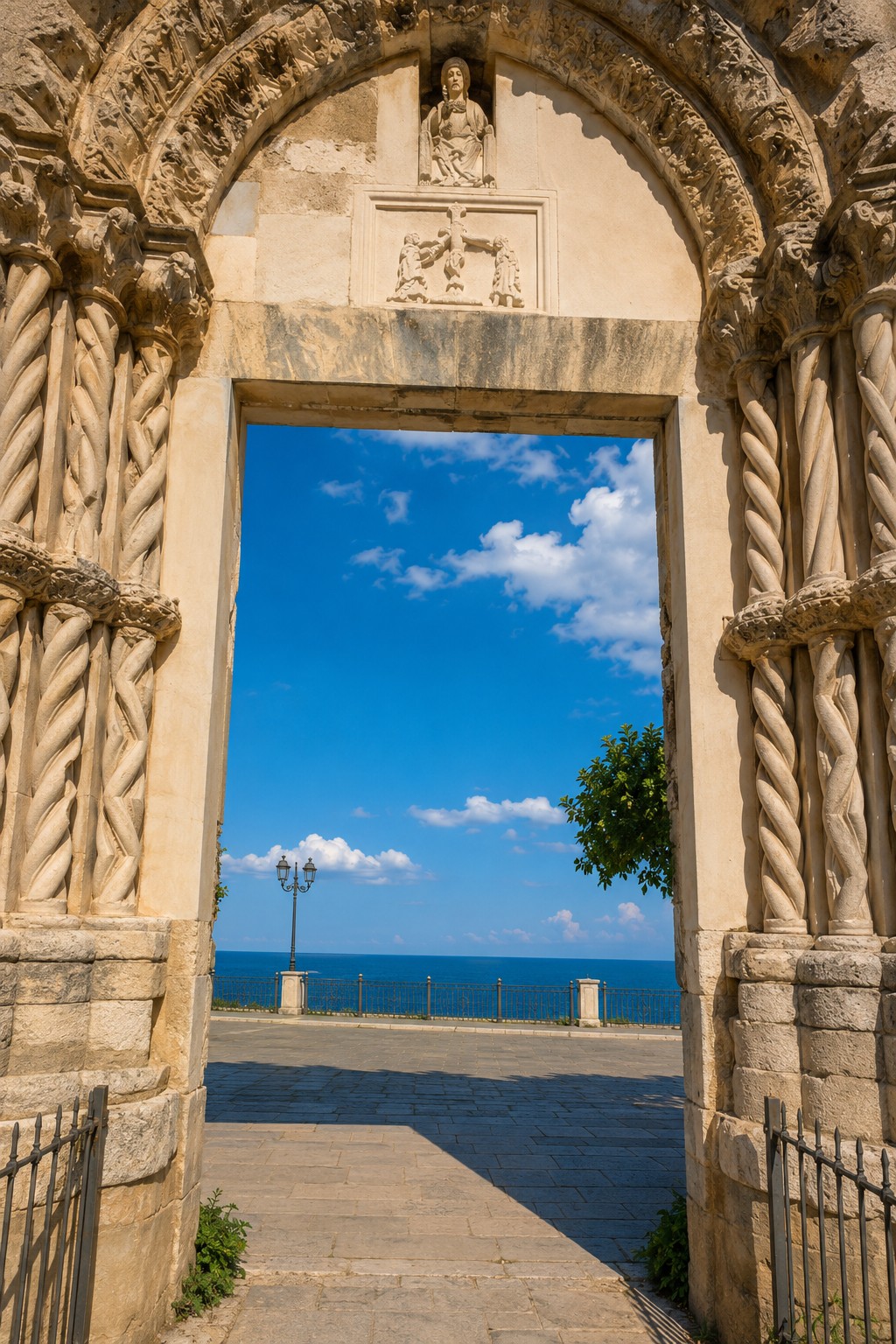 Portail roman sculpté du centre historique de Vasto, encadrant une vue sur la promenade et la mer Adriatique.