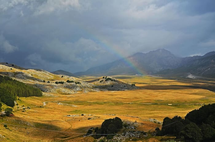 Un arc-en-ciel au-dessus du plateau de Campo Imperatore, entre les herbes dorées et les montagnes prises dans un ciel d'orage.