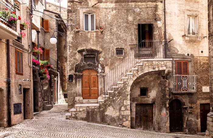 Ruelle pavée de Pacentro avec un escalier de pierre et des géraniums aux fenêtres.